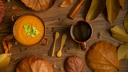 Autumn pumpkin soup with cup of brown tea on rustic table with dry leaves