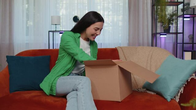 Portrait of happy girl unpacking delivery parcel sitting at home. Smiling satisfied young woman shopper, online shop customer opening cardboard box receiving purchase gift by fast postal shipping