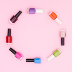 Colorful nail polish bottles oin circle make copy space frame on pastel pink backgorund. Flat lay