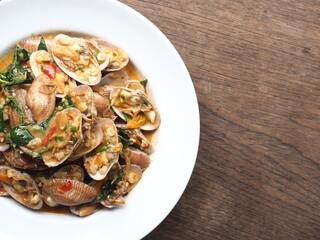 Top view dish of Thai stir fried clams in creamy chili paste sauce on wooden table
