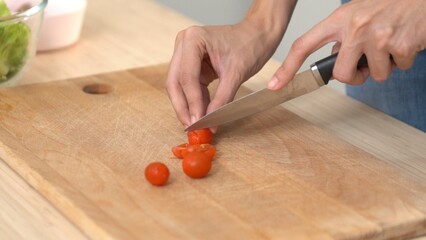 Close up hands holding a knife preparing a contented meal. Sliced tomatoes and other vegetables on...