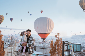 happy family looking at hot air balloon flying around them when visiting cappadocia turkey in winter - obrazy, fototapety, plakaty