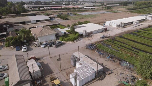 Aerial view of a tractor driving near fields of green plants in a kibbutz in northern Israel during the summer, mountains in the background, parallax to the left