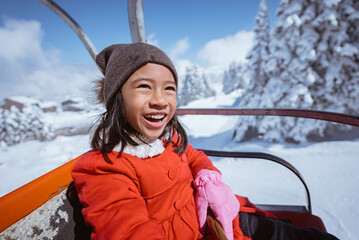 portrait of excited young girl riding a ski lift going up on top of the snowy mountain