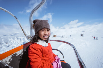 portrait of excited young girl riding a ski lift going up on top of the snowy mountain