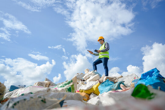 Male worker working at a recycling plant holding a tablet. Supervising work to dispose and recycle waste at a waste recycling plant that is a waste recycling business.
