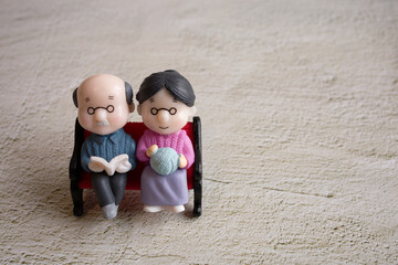 The elderly couples are sitting on the bench. The man is reading the book and the woman is knitting...