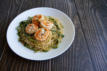 Stir-fried rice vermicelli and water mimosa with 4 prawns on the top of the white plate. Yummy food from Thailand.