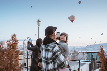 happy family looking at hot air balloon flying around them when visiting cappadocia turkey in winter