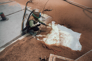 Male worker surface corrosion plate preparation by sandblasting bounce off of tank top deck.