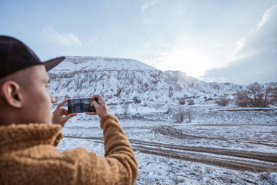 man taking picture of beautiful snowy scenery using his mobile phone