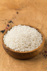 Raw round white rice in a wooden bowl on a wood background