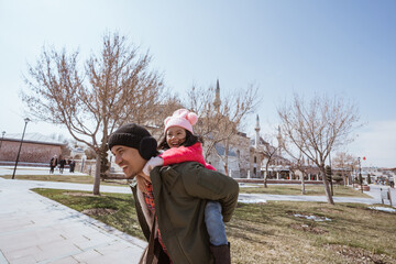 father carrying her daughter on his shoulder piggyback ride while visiting mosque in the city of...