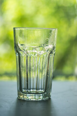 A faceted glass of water. Translucent glass on a nature blur background. Close up