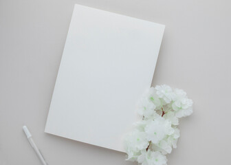 White invitation card mockup with a white flower on beige background, Minimal beige workplace composition, flat lay, mockup