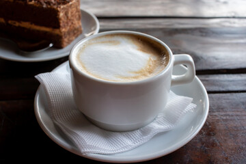 Cup of cappuccino and piece of cake on black wooden table. Cup of coffee with milk foam and dessert...