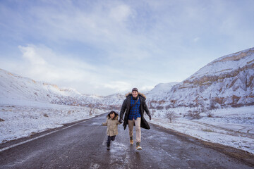 dad and daughter walking on empty street holding hand with majestic view of snowy valley