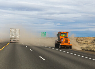 Road work or tractor vehicle driving on a dusty highway with semi truck and traffic