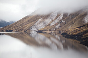 Low lying clouds over lake with snow dusted mountain