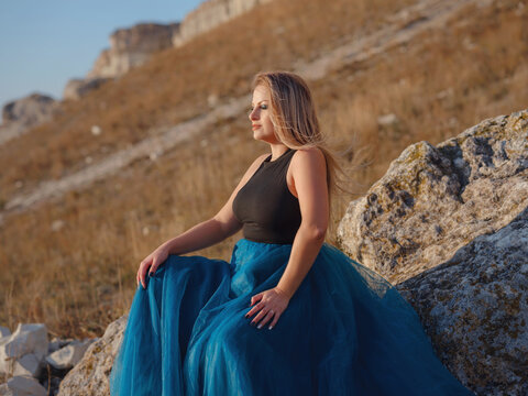 Fashionable woman on desert field near mountain wearing black top and blue tulle skirt
