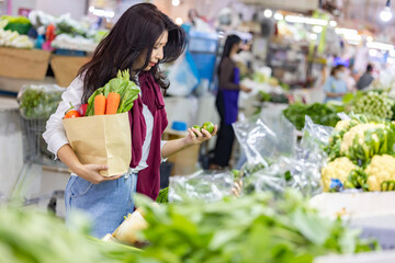 Asian woman shopping healthy food vegetables and fruits in supermarket. Woman choosing lemons at the grocery store, picks up lemons at the fruit and vegetable aisle in supermarket.