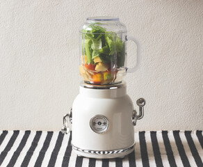 white vintage blender or smoothie maker withe vegetables, tomatos, apples and water   on  black and...