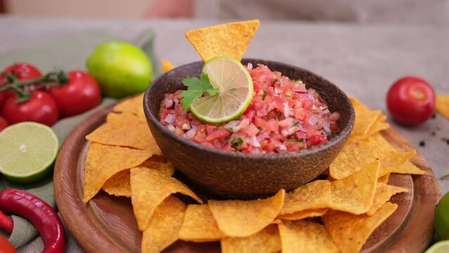 woman puts nacho chip into salsa dip sauce in wooden bowl