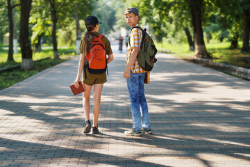portrait of students in a city park, teenage schoolchildren a boy and a girl walking along a path, rear view - Powered by Adobe