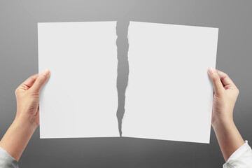 Hands tearing a sheet of white paper on gray background.