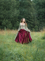 Fototapeta premium Beautiful happy woman in long medieval dress walking on the field