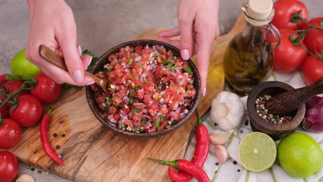 woman mixing salsa dip sauce ingredients in wooden bowl