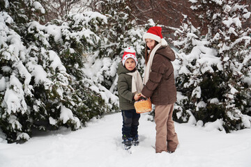 Fototapeta na wymiar Cute happy kids, boy and girl in santa hats decorate christmas tree in snowy forest.