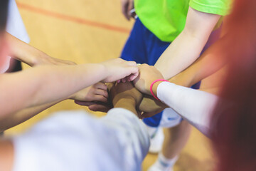 Team of kids children basketball players stacking hands in the court, sports team together holding hands getting ready for the game, playing indoor basketball, team talk with coach, close up of hands