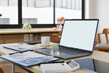 Empty screen of laptop computer place on office desk with business chart, data sheet, tablet, coffee cup and calculator.