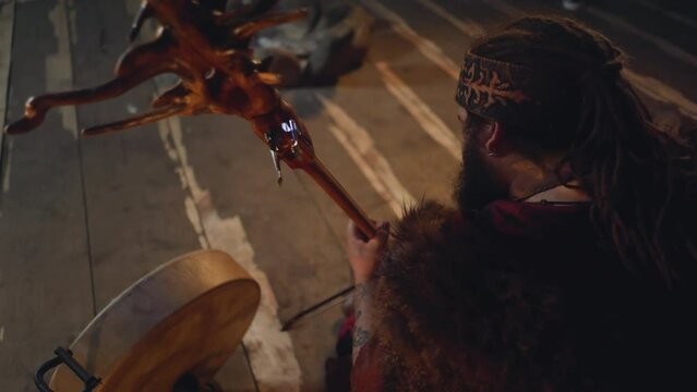 Man with fur on shoulders plays stylish string instrument on rustic stage backside view. Siberian musician presents traditional music