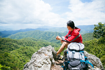 Young person hiking female sitting on top rock, Backpack woman looking at beautiful mountain valley at sunlight in summer, Landscape with sport girl, high hills, forest, sky. Travel and tourism. - Powered by Adobe