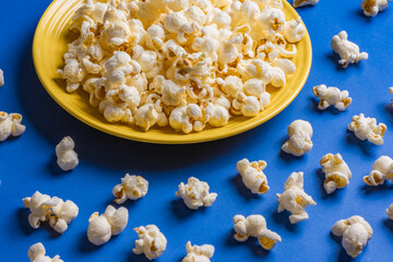 Obraz na płótnie Canvas Popcorn on a yellow plate on blue background, Food or snack, Health or salt