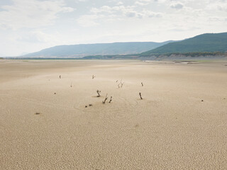 Arid landscape due to lack of rain. Extreme drought, cracked soil and dead trees. In the background mountains with forests and a river with little flow. Concept climate change and drought.