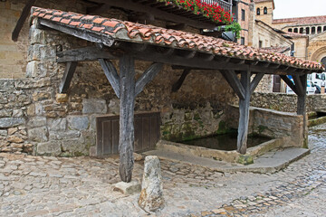 The water fountain and wash house with roof where, in the past, the women would wash clothes and the church in the background in the old medieval town of Santillana del Mar.