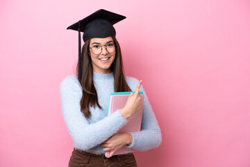 Young student Brazilian woman wearing graduated hat isolated on pink background pointing to the side to present a product