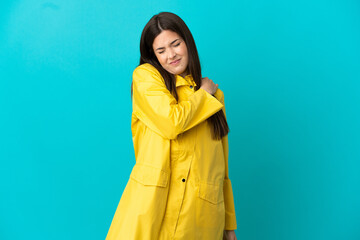 Teenager Brazilian girl wearing a rainproof coat over isolated blue background suffering from pain in shoulder for having made an effort