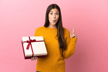 Teenager Brazilian girl holding a gift over isolated pink background intending to realizes the solution while lifting a finger up