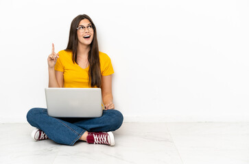 Young woman with a laptop sitting on the floor intending to realizes the solution while lifting a finger up