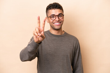 Young Brazilian man isolated on beige background smiling and showing victory sign