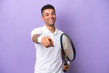 Young Brazilian man isolated on purple background playing tennis and pointing to the front