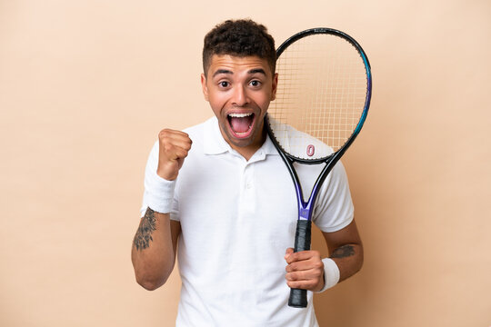 Young Brazilian Handsome Man Playing Tennis Isolated On Beige Background Celebrating A Victory In Winner Position