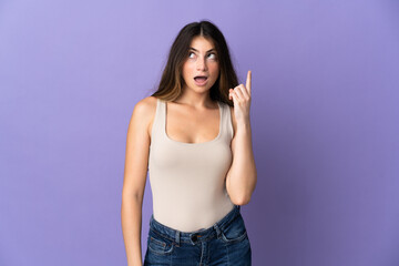 Young caucasian woman isolated on purple background thinking an idea pointing the finger up