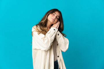 Young caucasian woman isolated on blue background making sleep gesture in dorable expression