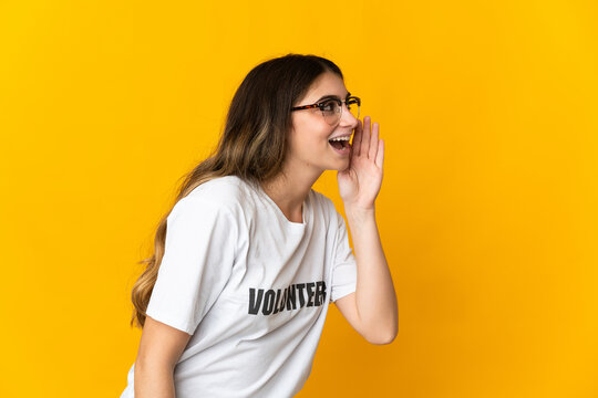 Young volunteer woman isolated on yellow background shouting with mouth wide open to the side