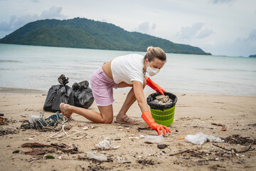 A female ecologist volunteer cleans the beach on the seashore from plastic and other waste